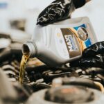 Close-up of a mechanic pouring engine oil into a car engine, highlighting maintenance work.