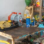 A cluttered workbench in an automobile garage with tools, oil cans, and maintenance products.