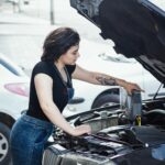 Woman adding oil to a car engine outdoors in Rasht, Iran, showcasing DIY vehicle care.