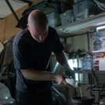 Man pours engine fluid into a vehicle in a dimly lit garage.